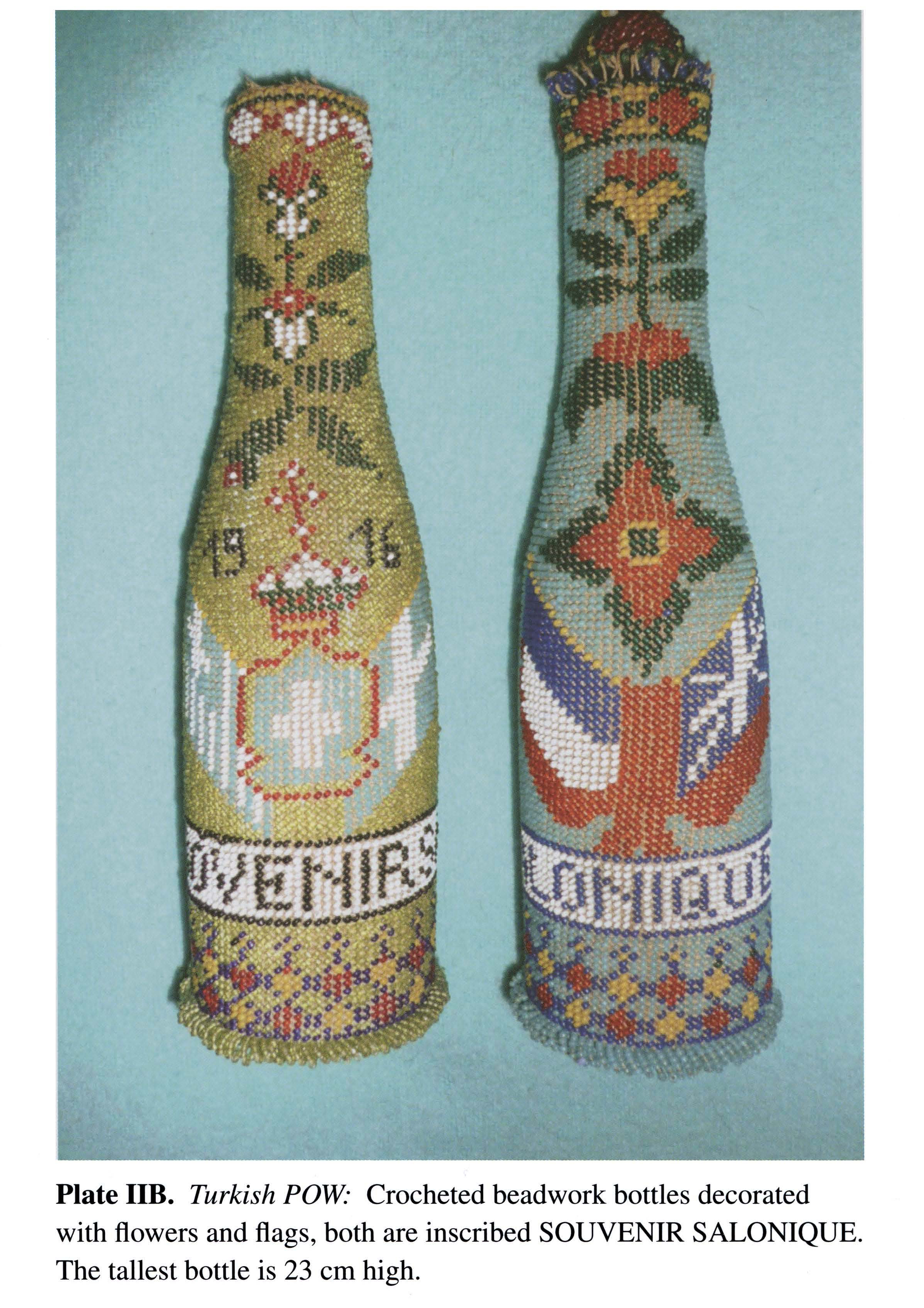 Plate IIB Turkish POW- Crocheted beadwork bottles decorated with flowers and flags, both are inscribed SOUVENIR SALONIQUE. The tallest bottle is 23 cm high.