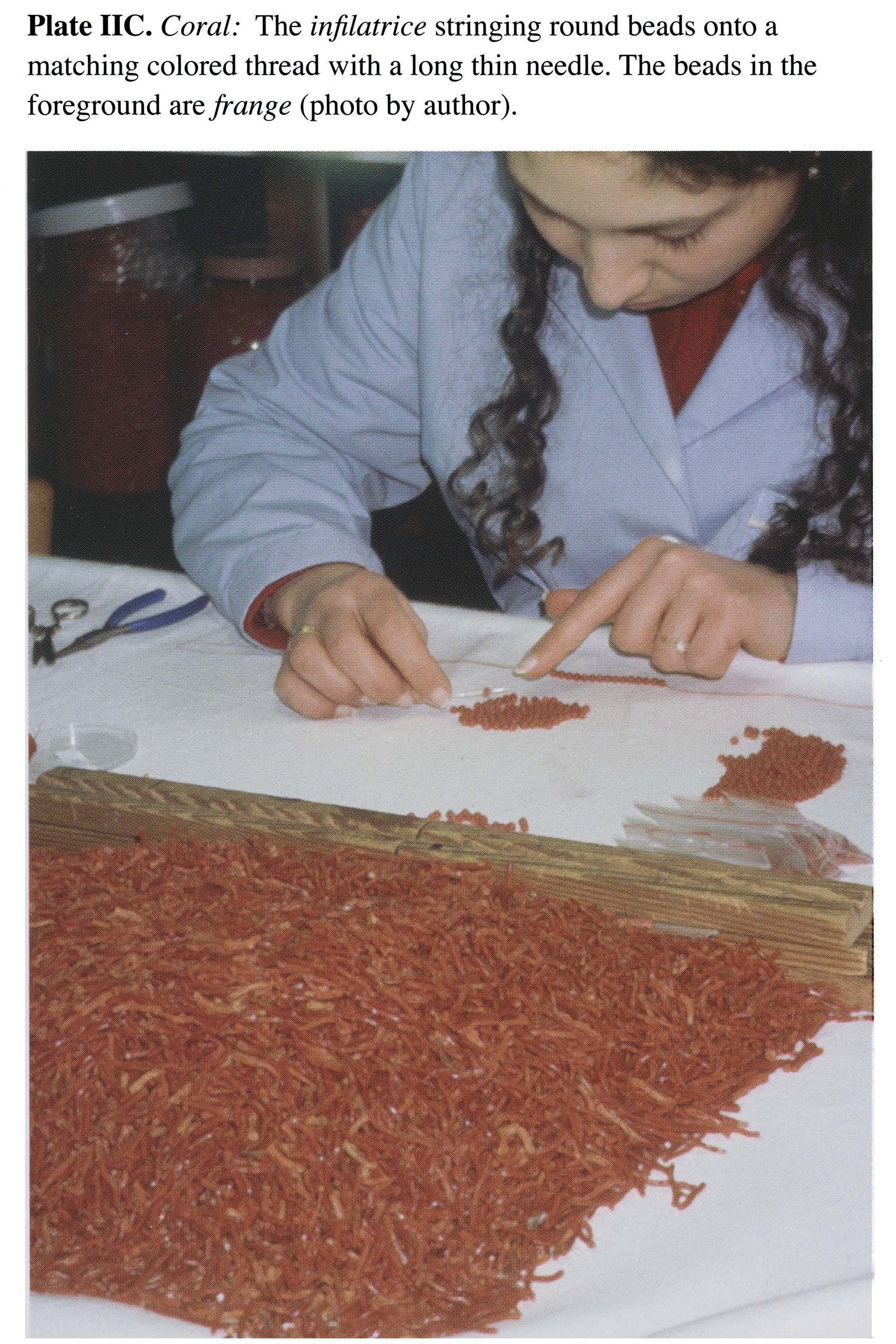 Plate IIC Coral: The infilatrice stringing round beads onto a matching colored thread with a long thin needle. The beads in the foreground are frange (photo by author).